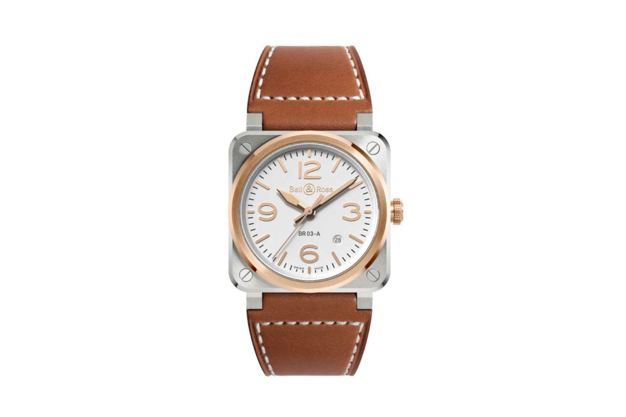 A warm watch with a brown leather strap, a square silver bezel surrounding a golden circular bezel, and a white dial.