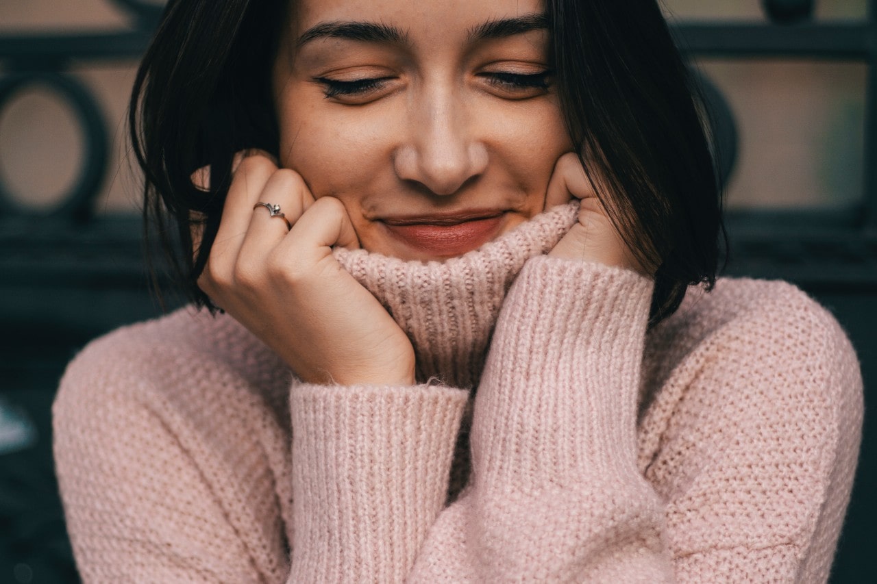 A woman in a pink turtleneck sweater cozies up inside.
