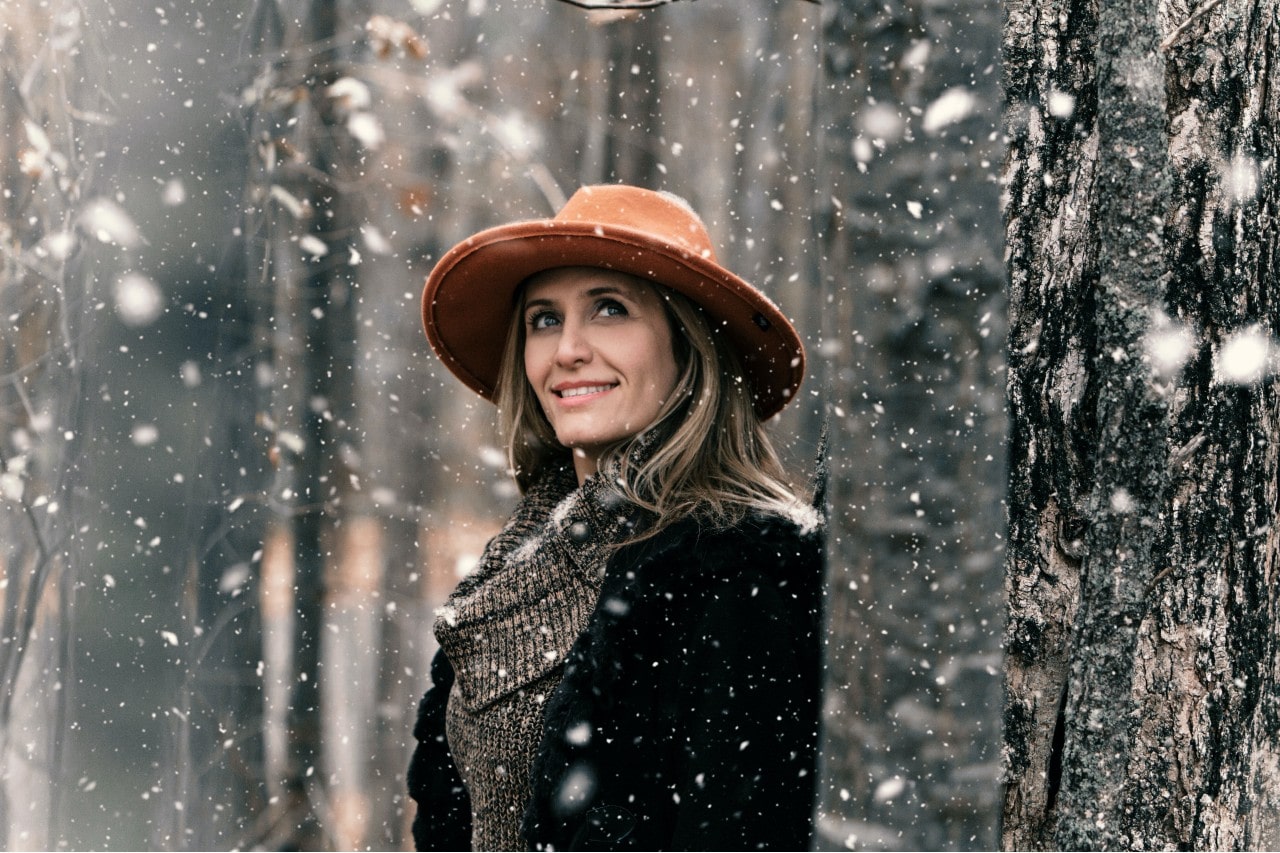 A woman bundled up walks through snowfall in a winter forest.