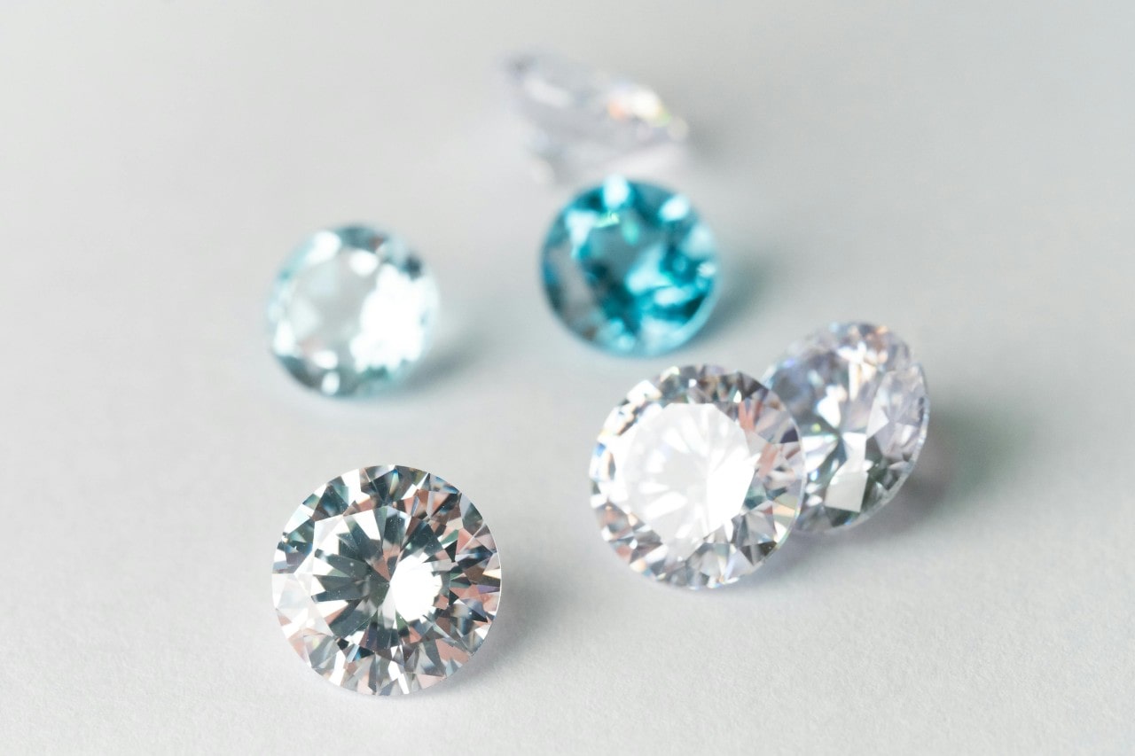 Several sparkling diamonds, including clear and blue ones, are scattered on a light surface.