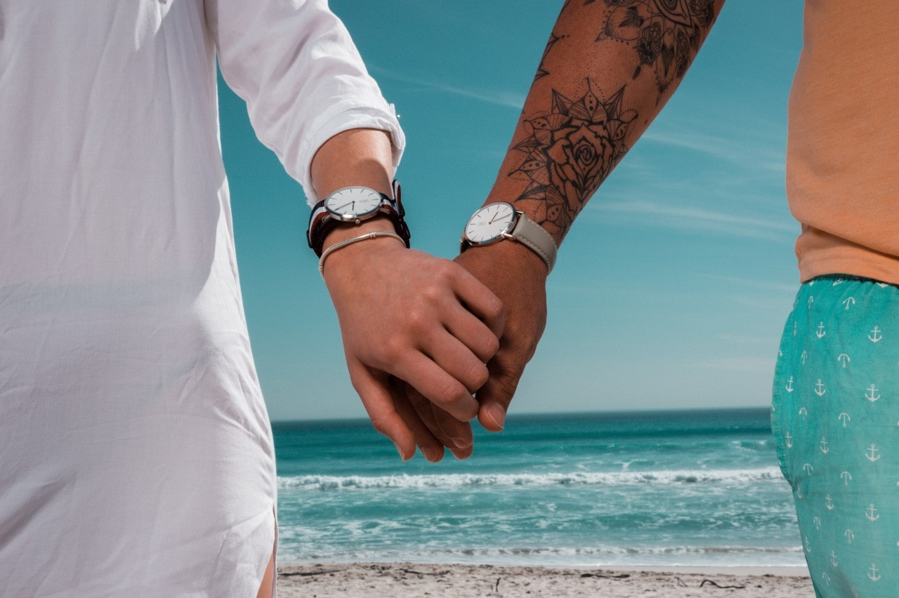a couple holding hands on the beach and wearing luxury watches