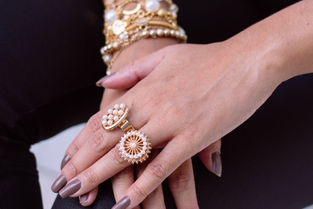 A woman with multiple bold yellow gold and pearl rings along with several bracelets along her wrist