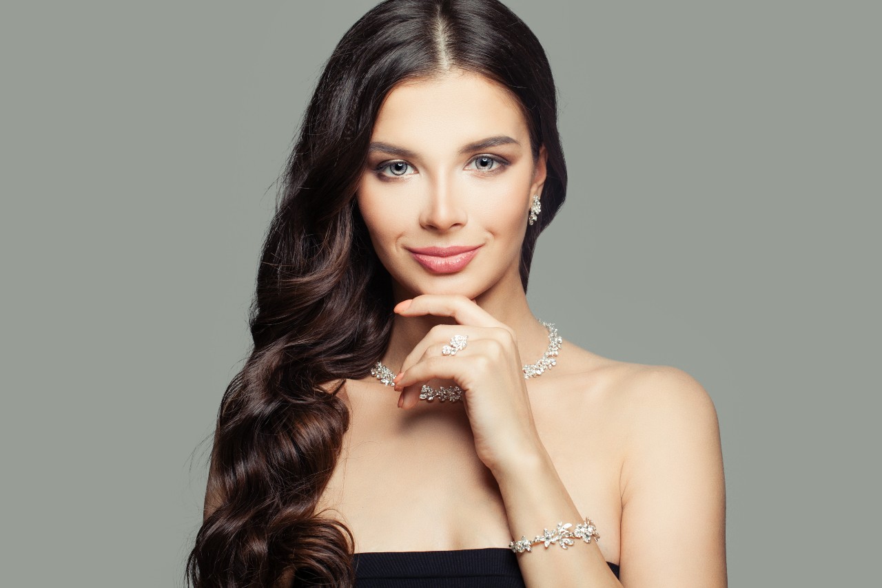 A picture of a woman with long wavy hair and a strapless black top, showcasing a diamond floral jewelry set, including earrings, collar necklace, a ring, and a bracelet. A picture of a woman with long wavy hair and a strapless black top, showcasing a diamond floral jewelry set, including earrings, collar necklace, a ring, and a bracelet.