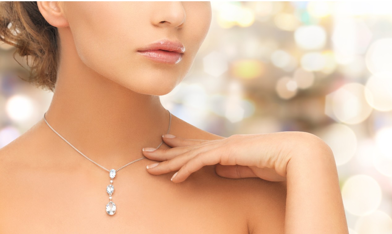 A close-up of a woman wearing a three-stone drop diamond necklace with a soft bokeh background. A close-up of a woman wearing a three-stone drop diamond necklace with a soft bokeh background.