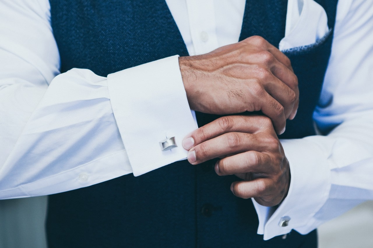 A close up of a man fixing silver cufflinks on his white shirt