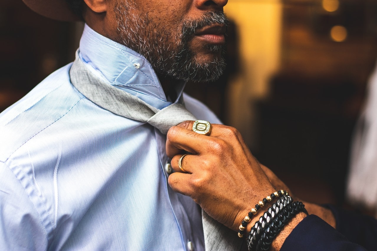 A hand adorned with chain bracelets and statement rings fixing a tie on a man in a blue shirt