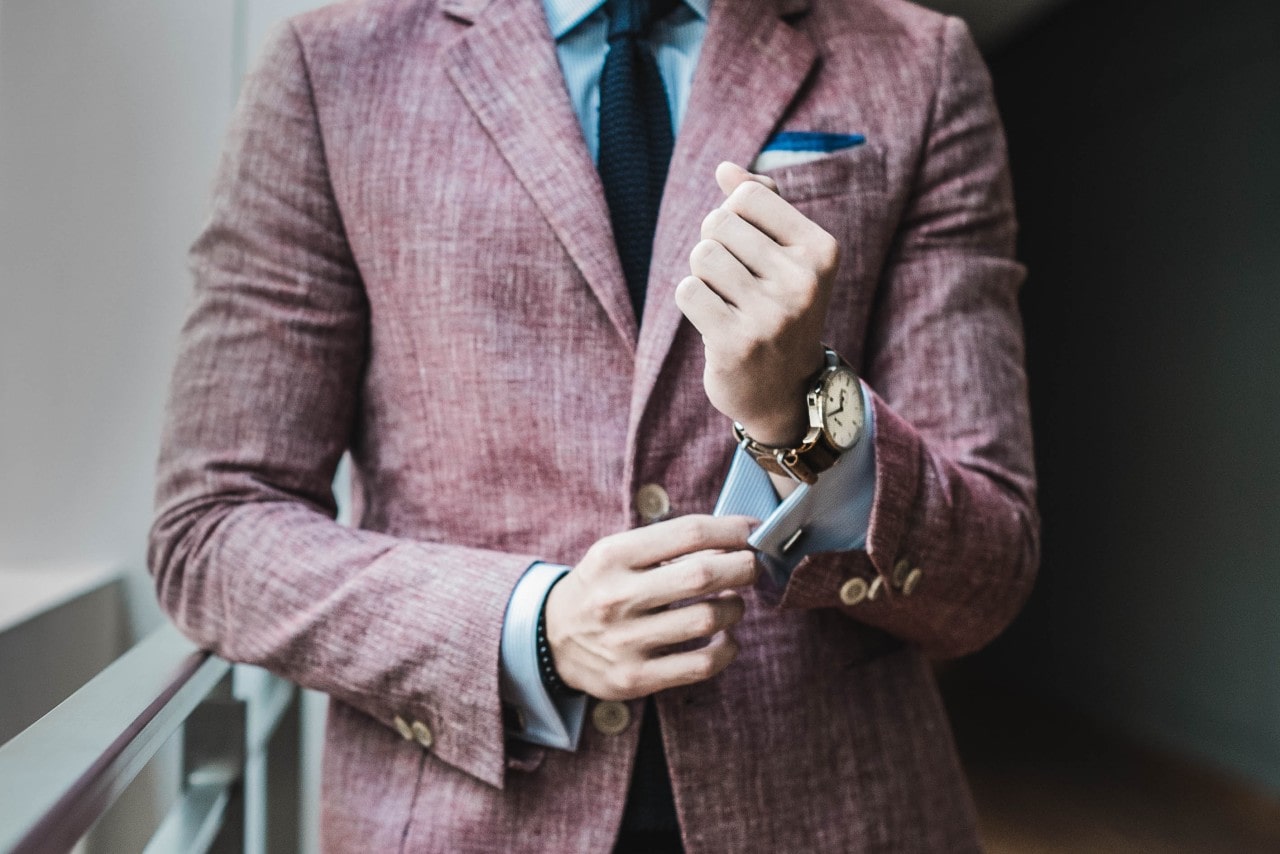 A man in pink suit fixing his cuffs, showcasing brown leather wristwatch