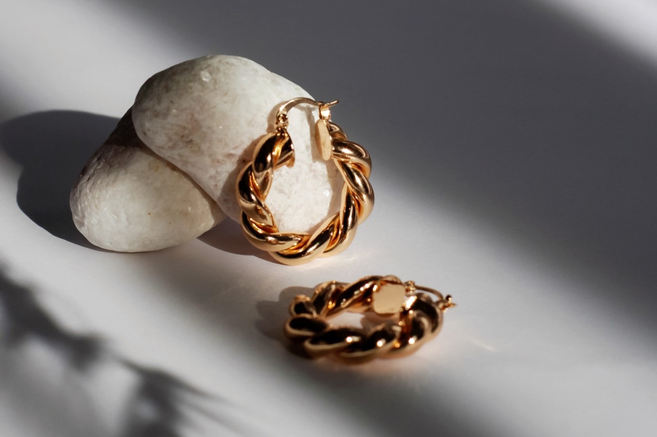 A pair of gold huggies earrings leaning against a white rock.