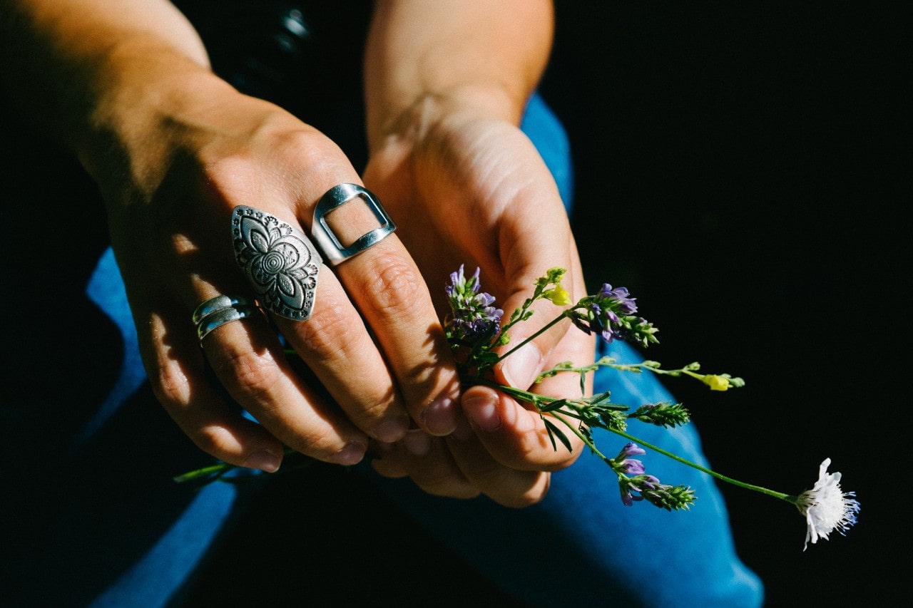 A woman wearing sterling silver fashion rings holds wildflowers.