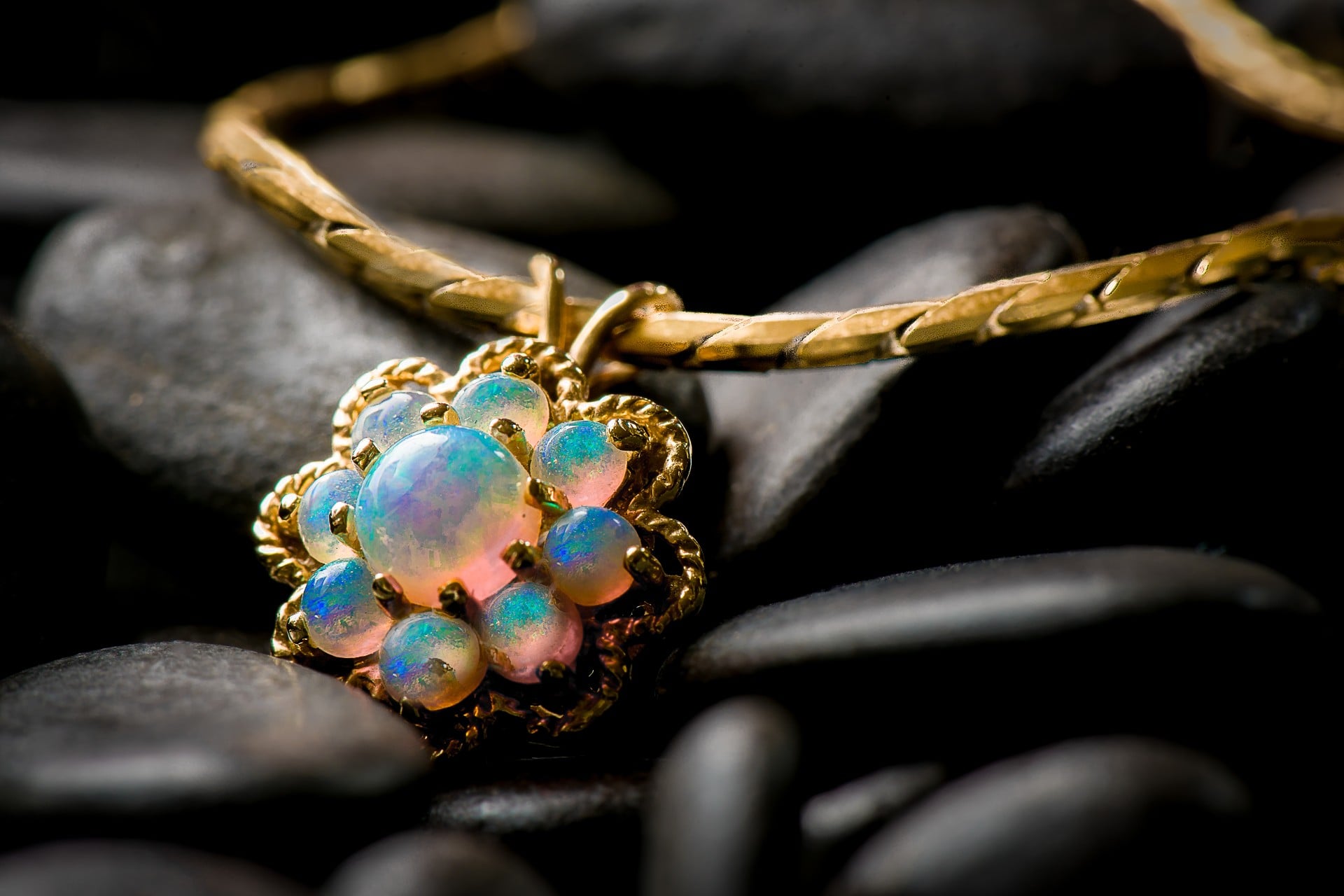 A yellow gold, floral-inspired opal pendant lays on black rocks.