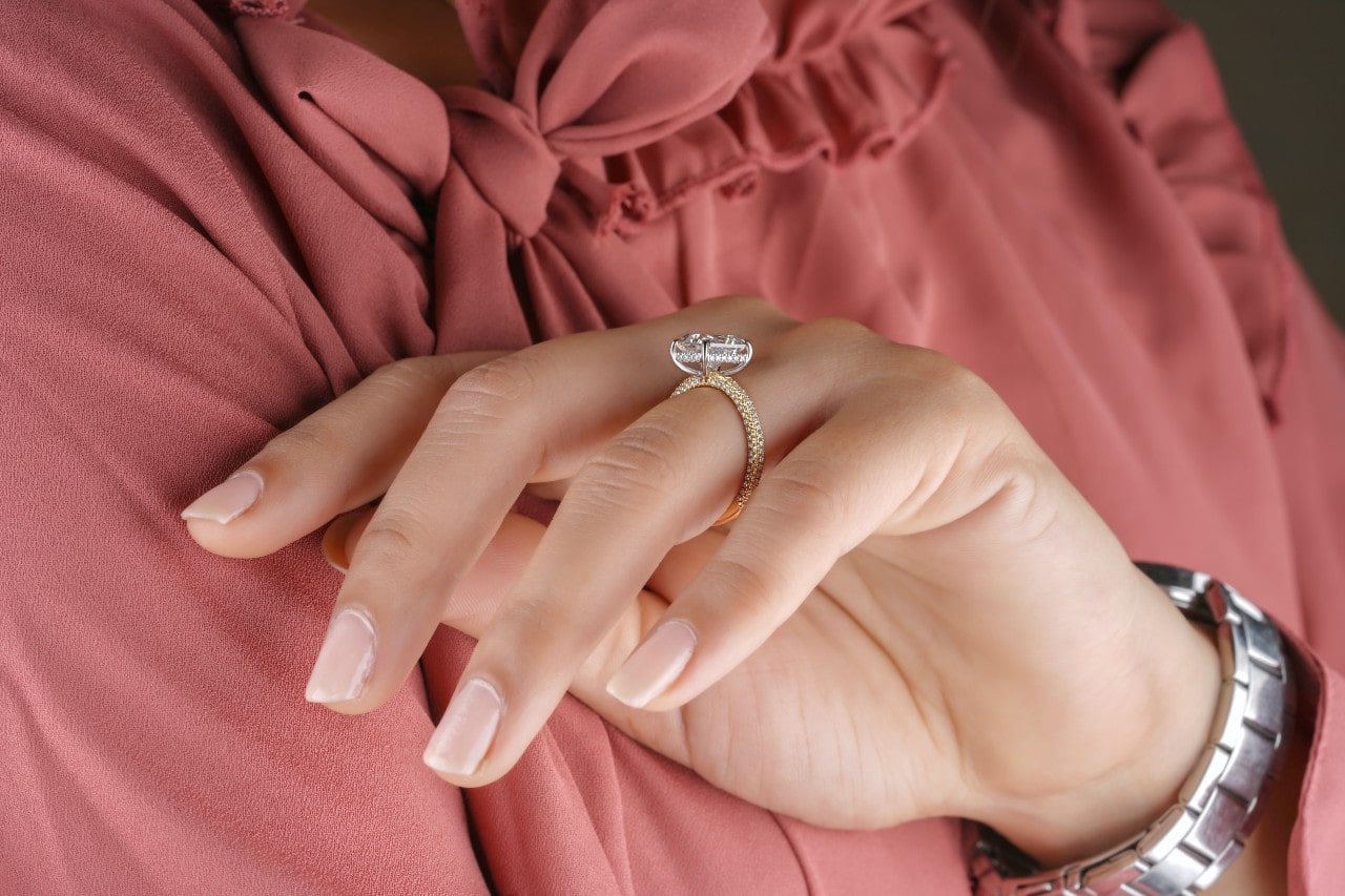 Close-up image of a woman wearing a radiant cut engagement ring and a pink blouse