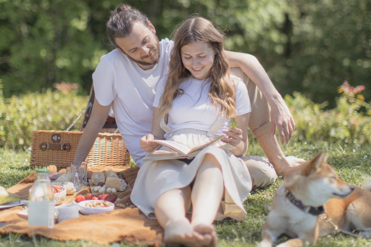 a man and woman having a picnic, wearing white, and reading a book together a man and woman having a picnic, wearing white, and reading a book together