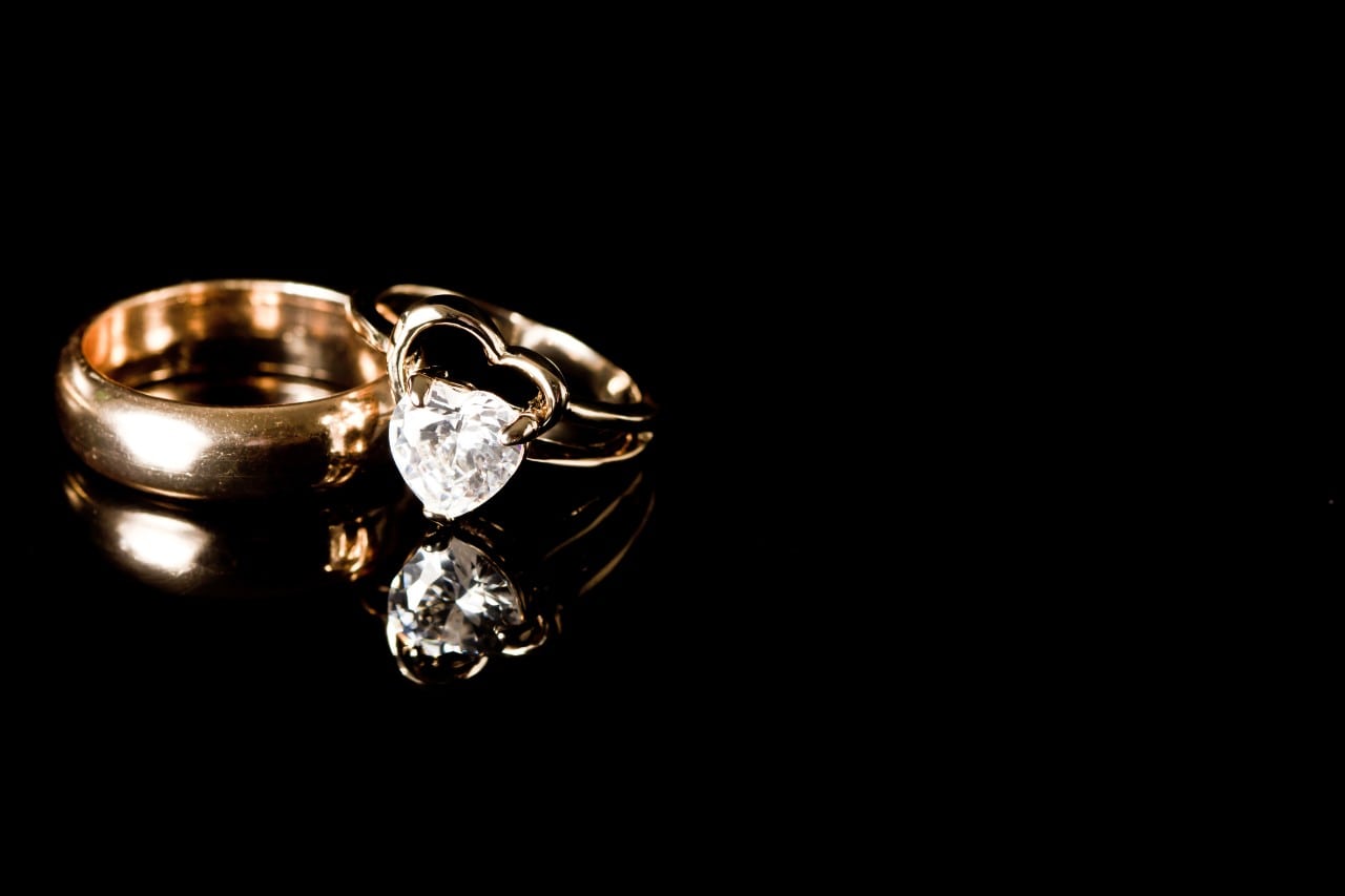 a yellow gold wedding band and engagement ring set against a black background a yellow gold wedding band and engagement ring set against a black background