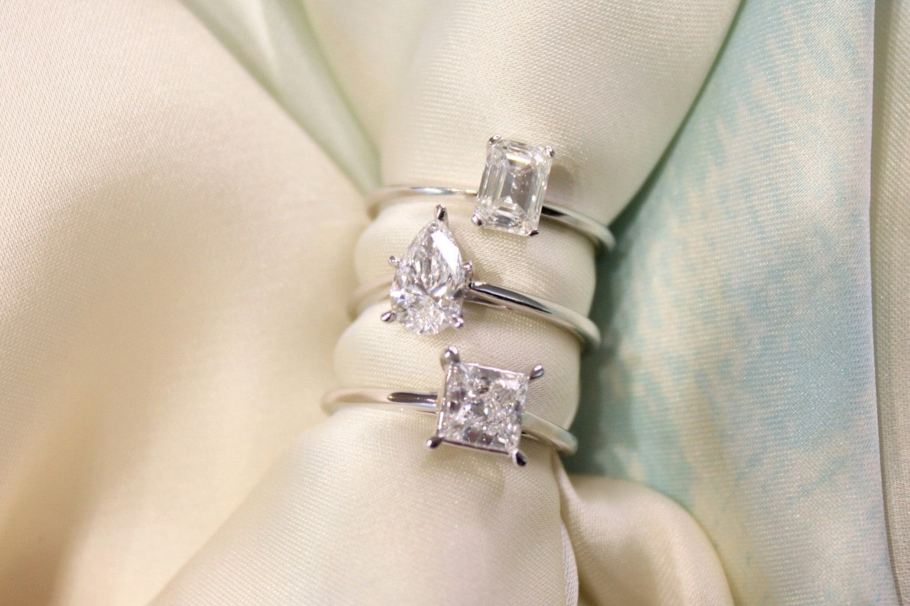 three silver solitaire engagement rings stacked on a piece of ivory fabric three silver solitaire engagement rings stacked on a piece of ivory fabric