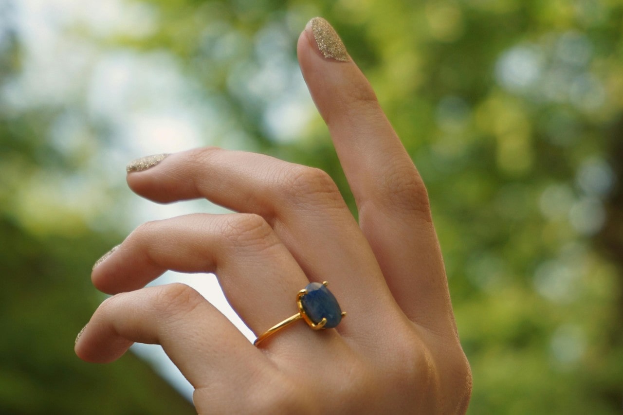 a woman’s hand raised to the sky, adorned with a yellow gold solitaire engagement ring with a blue stone a woman’s hand raised to the sky, adorned with a yellow gold solitaire engagement ring with a blue stone