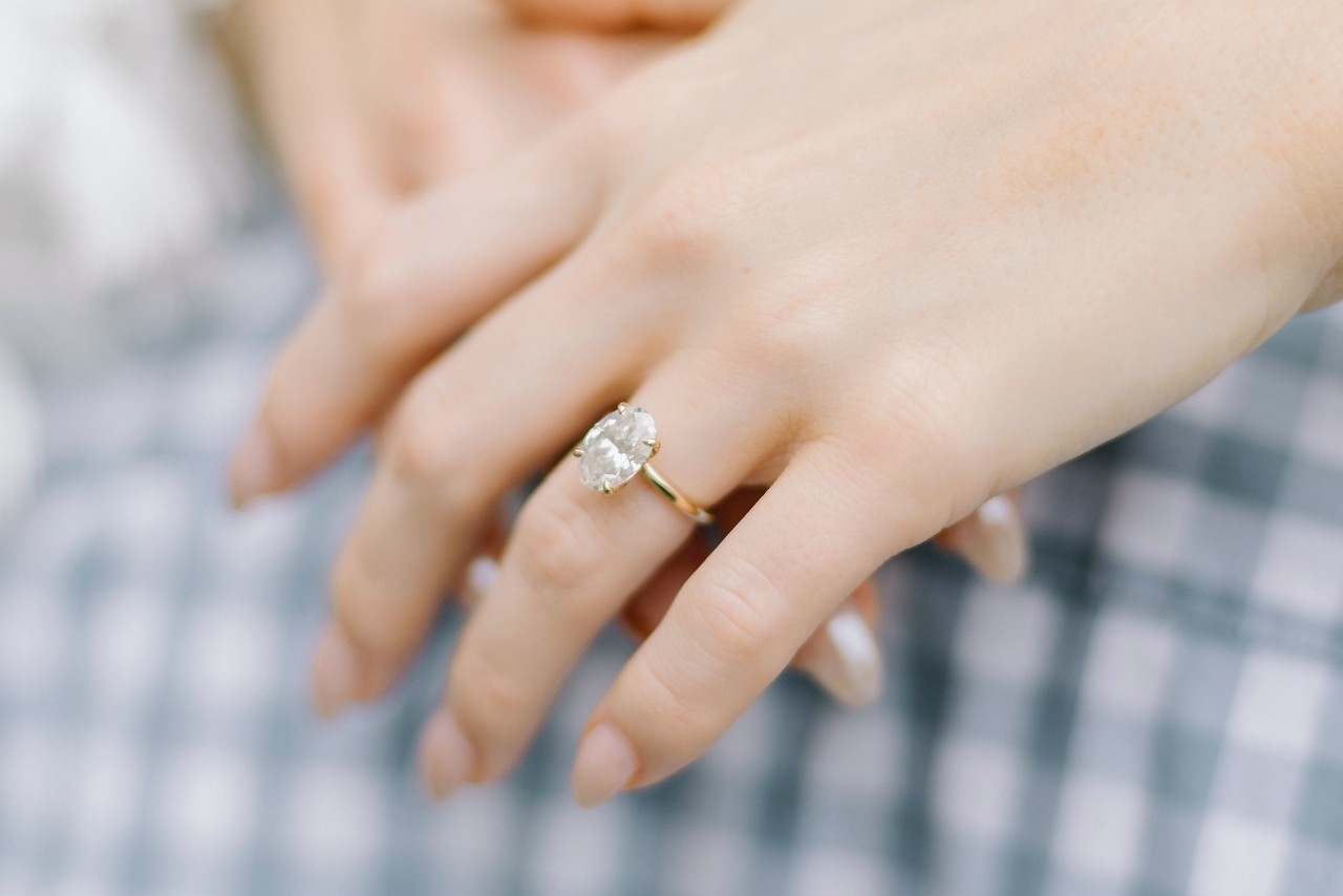 A woman hugs her partner, wearing an oval-cut solitaire ring.