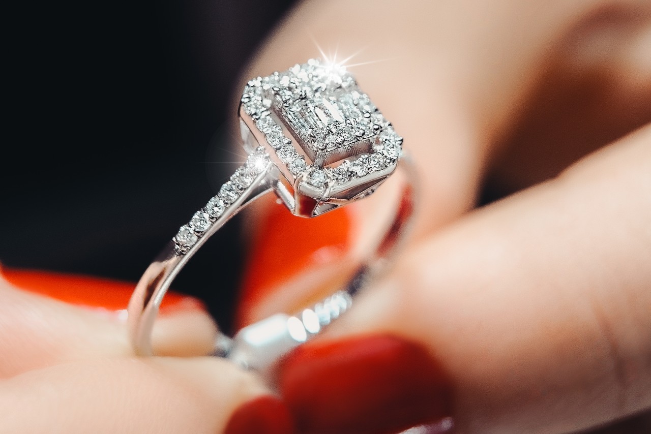 A woman with red nails holds a classic halo engagement ring.