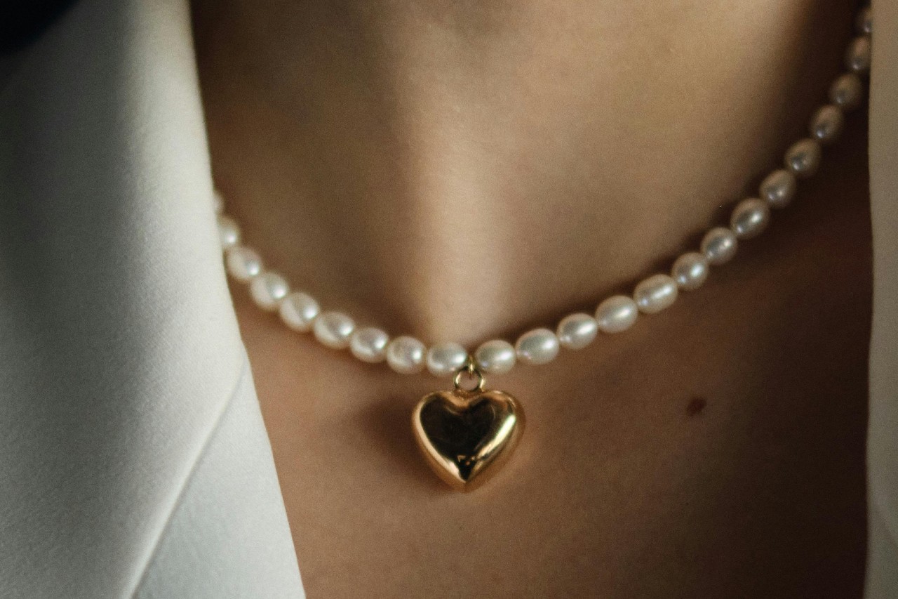 close up image of a woman’s neckline adorned with a pearl necklace and a yellow heart pendant close up image of a woman’s neckline adorned with a pearl necklace and a yellow heart pendant
