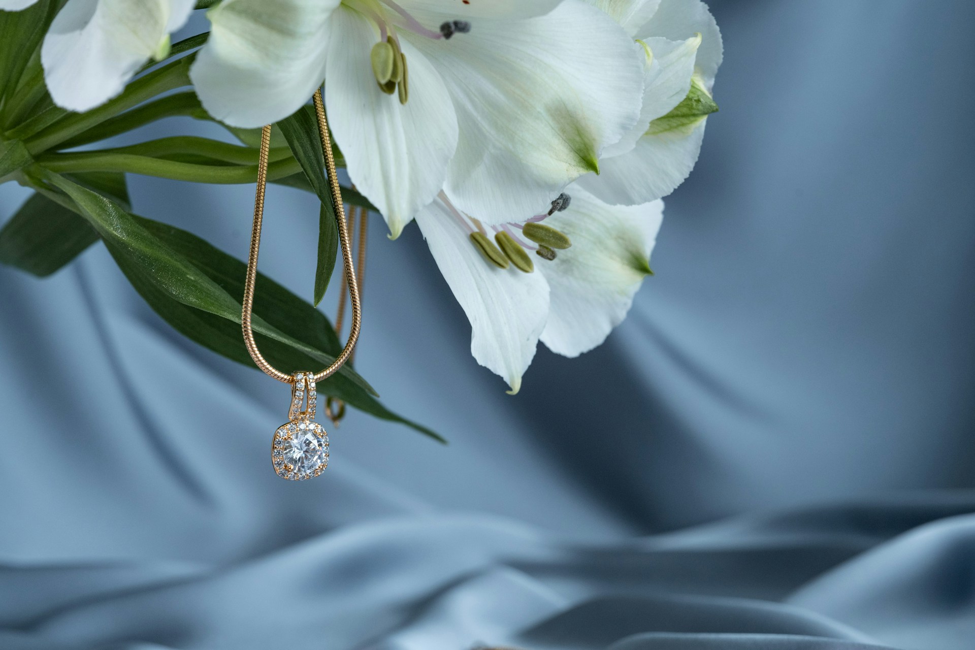 a yellow gold diamond halo pendant necklace hanging from a bouquet of white flowers