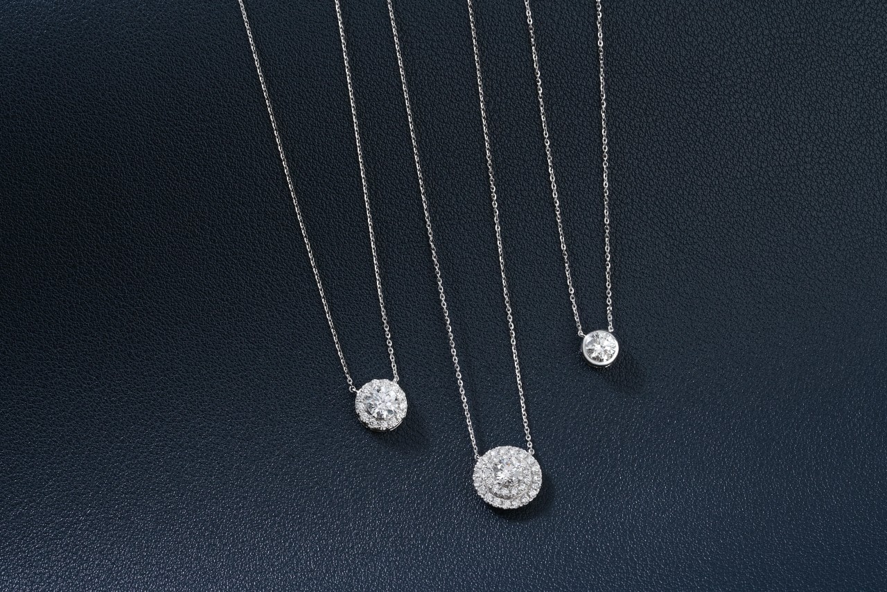 three diamond pendant necklaces wrought in silver on a black surface