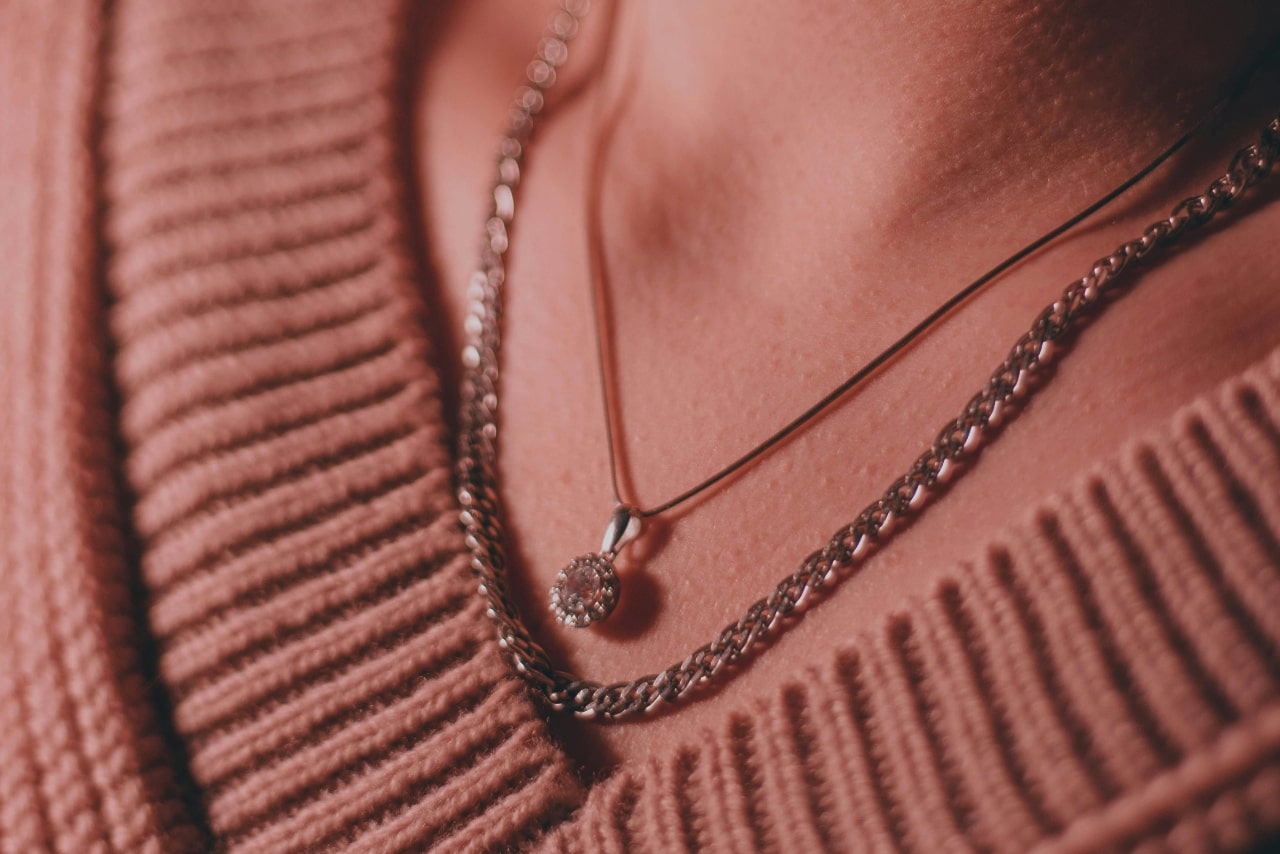 close up image of a woman’s neckline adorned with a diamond pendant necklace and a chain necklace