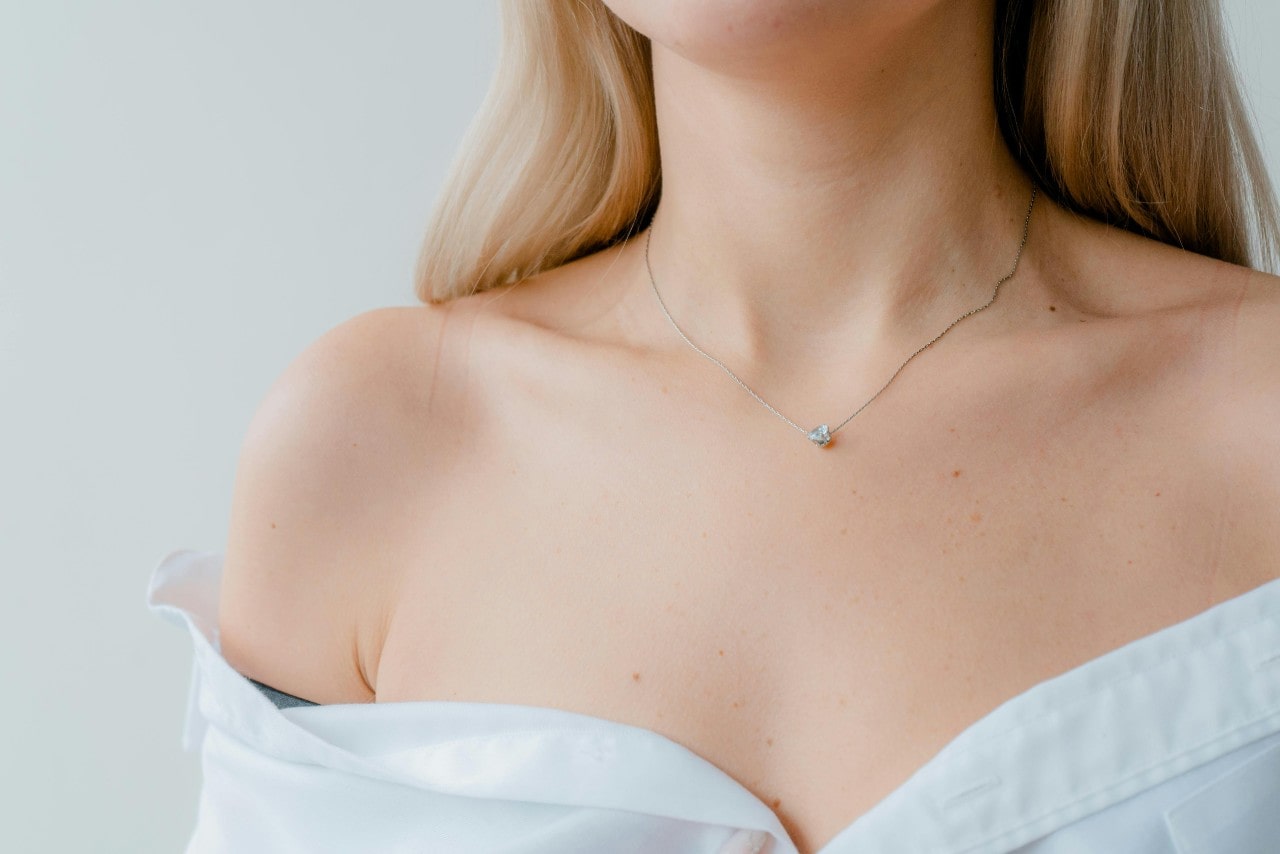 a woman wearing an open white blouse and a small diamond solitaire pendant necklace