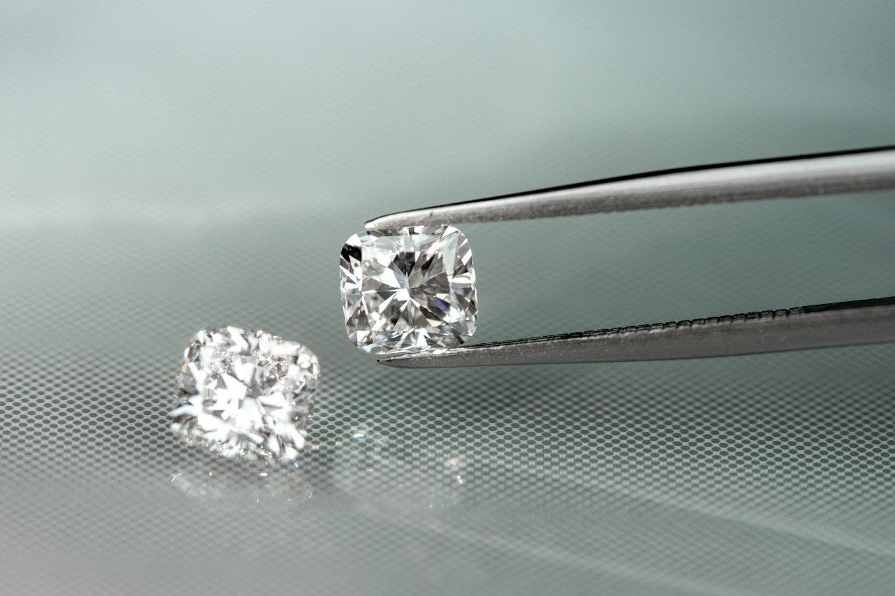 A pair of loose diamonds, with one being held by tweezers against a light reflective surface.