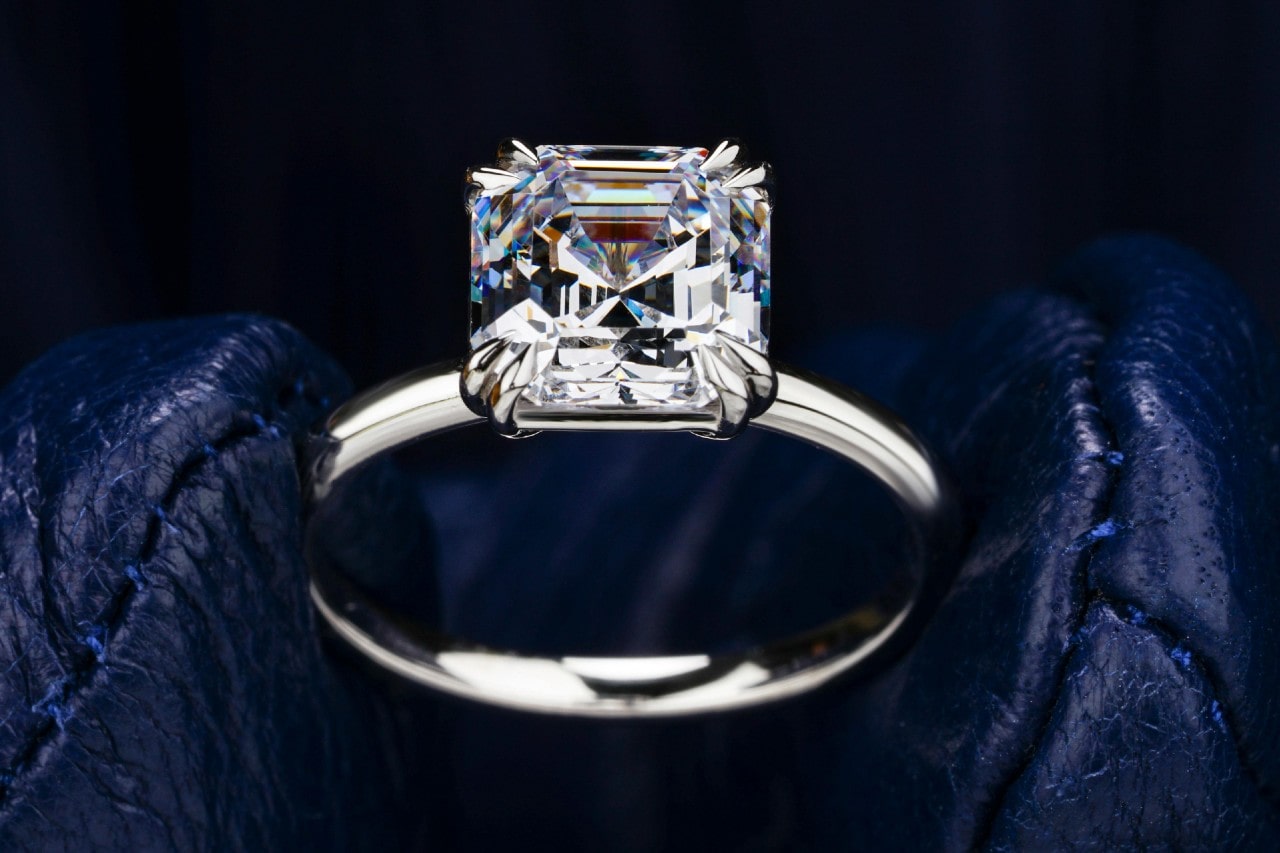 A close-up of an asscher cut solitaire engagement ring on a dark leather backdrop. A close-up of an asscher cut solitaire engagement ring on a dark leather backdrop.