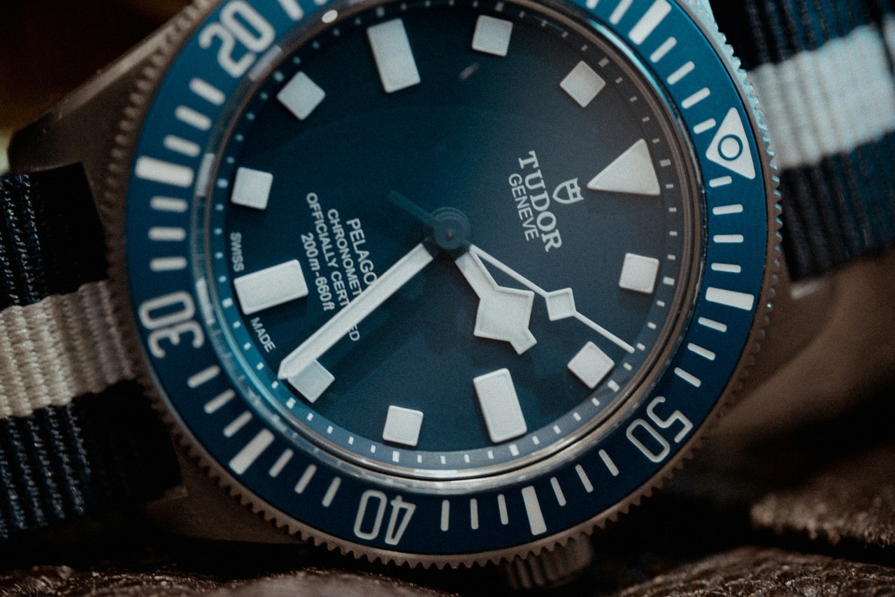 A close-up of a sporty TUDOR watch with a fabric strap displayed on its side.