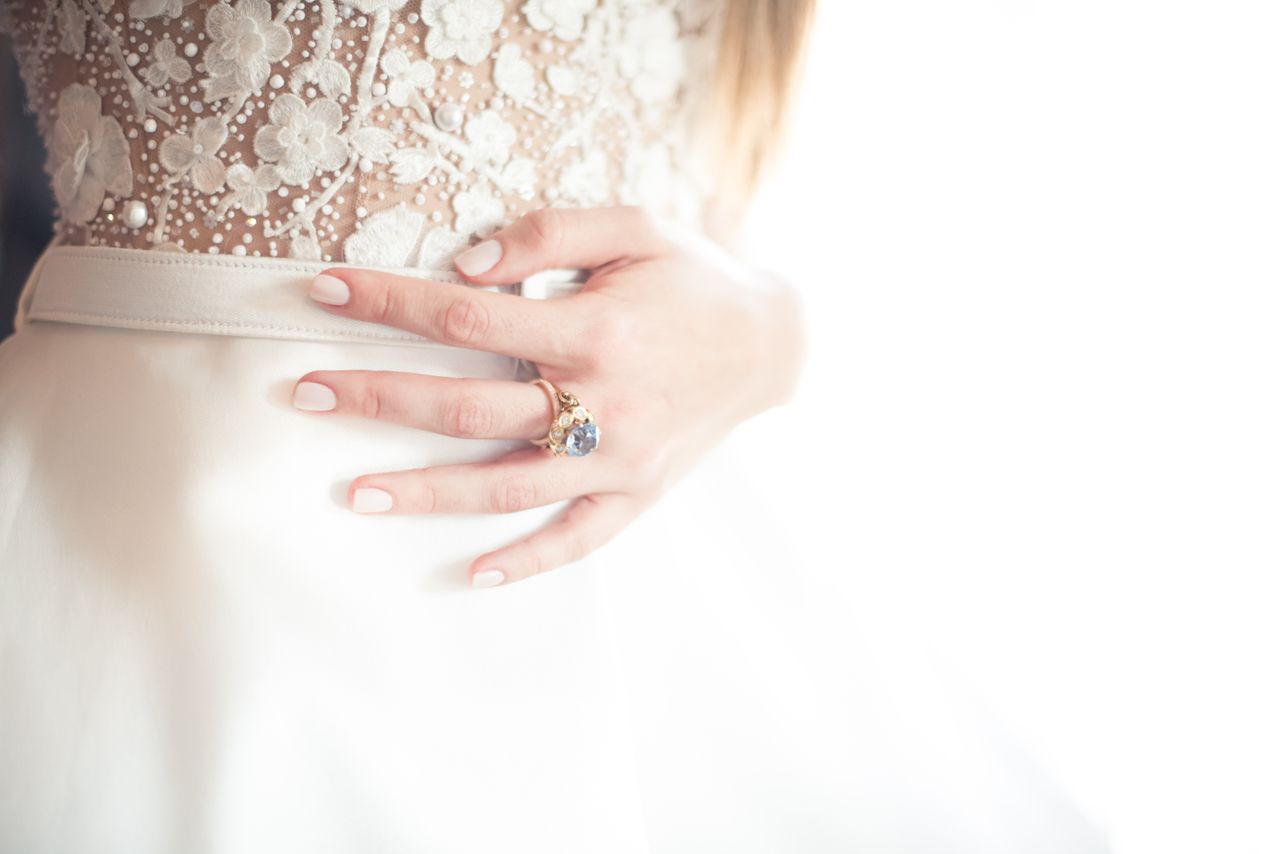 A bride rests her hand on her waist, wearing a gemstone engagement ring. A bride rests her hand on her waist, wearing a gemstone engagement ring.